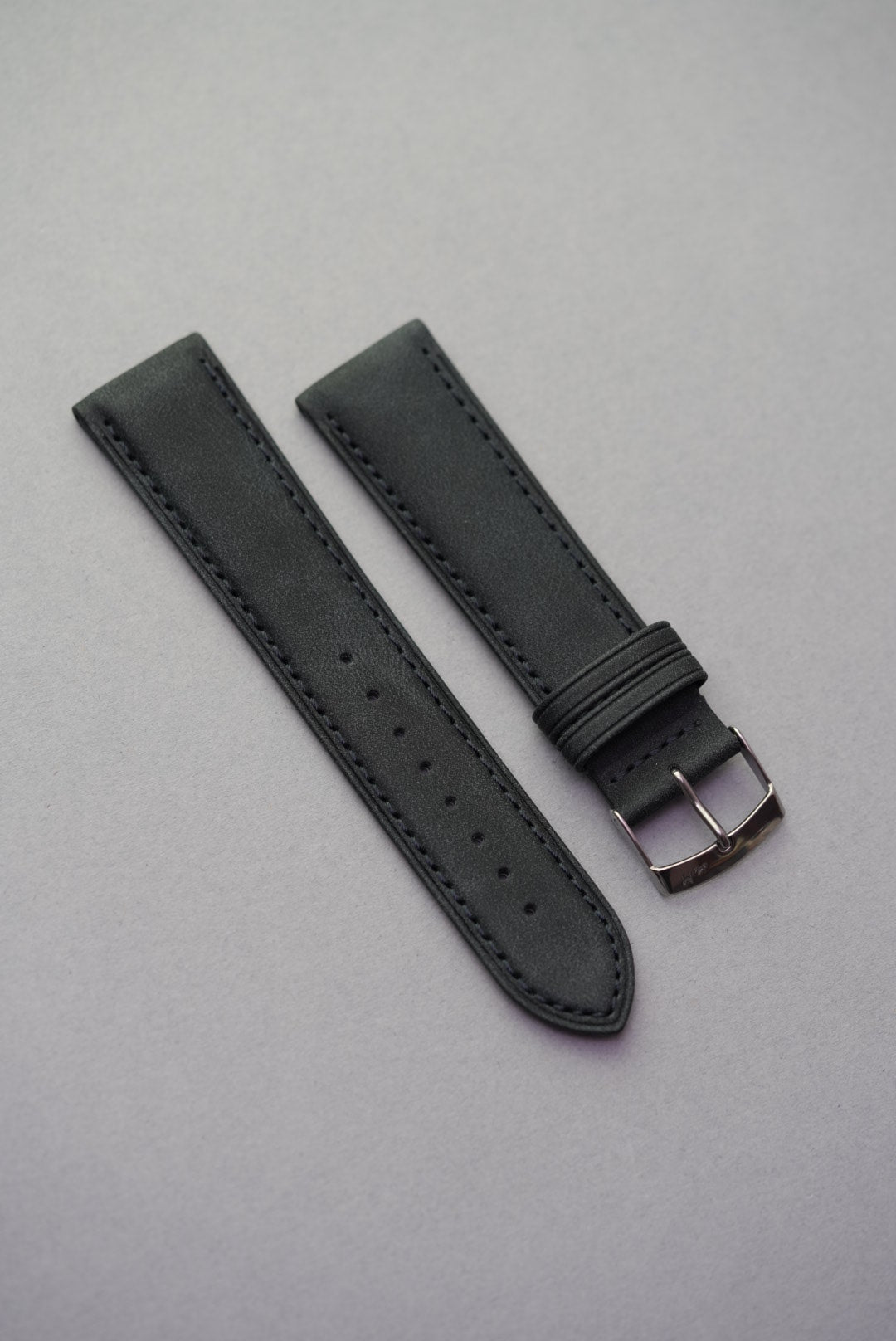Black suede watch strap laid out with polished buckle and even stitching.