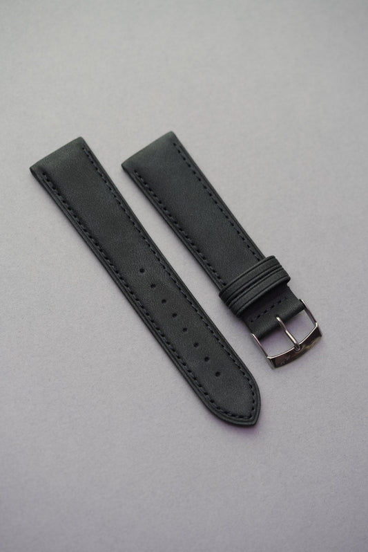 Black suede watch strap laid out with polished buckle and even stitching.