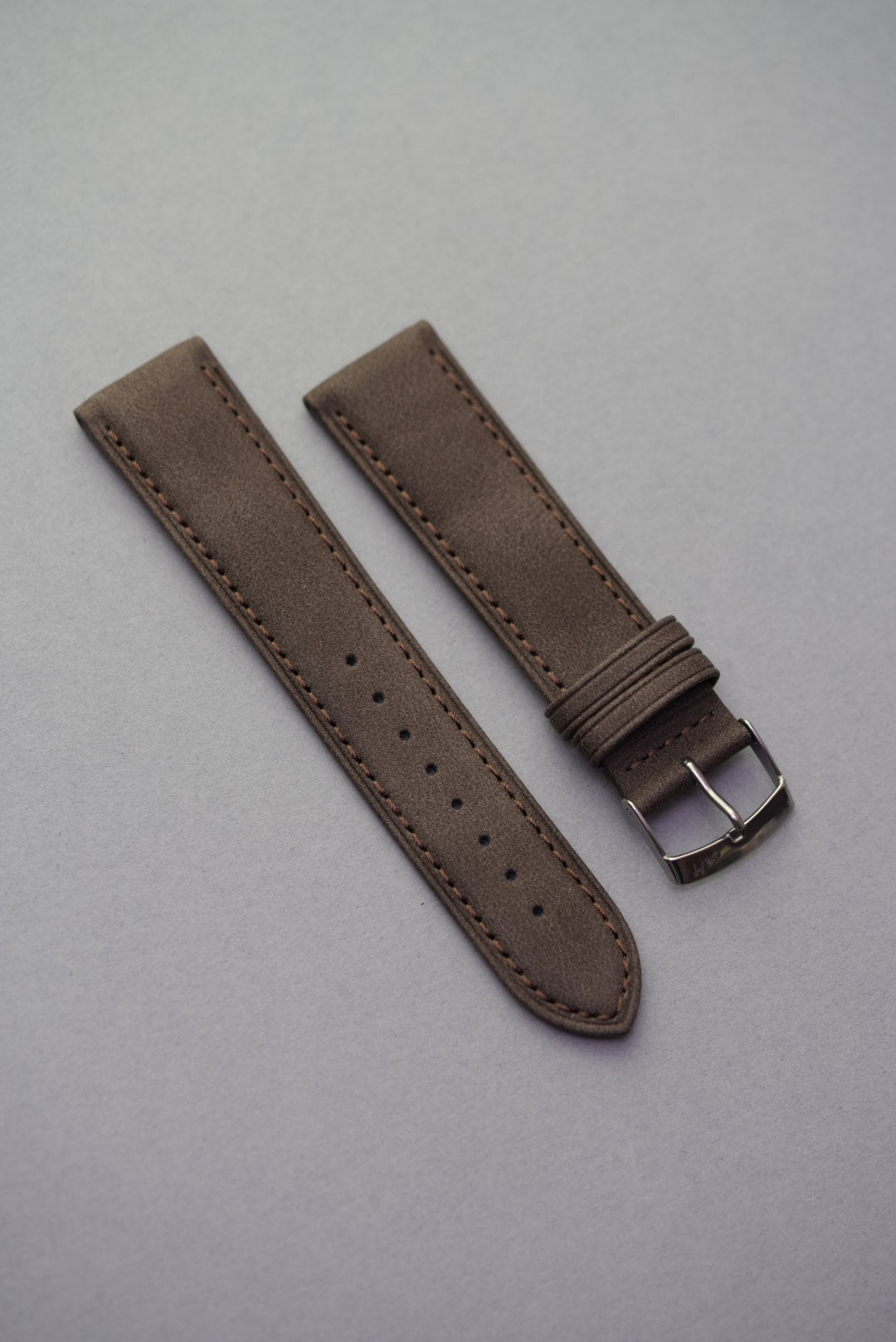 Dark brown suede watch strap laid flat showing clean stitching and buckle.