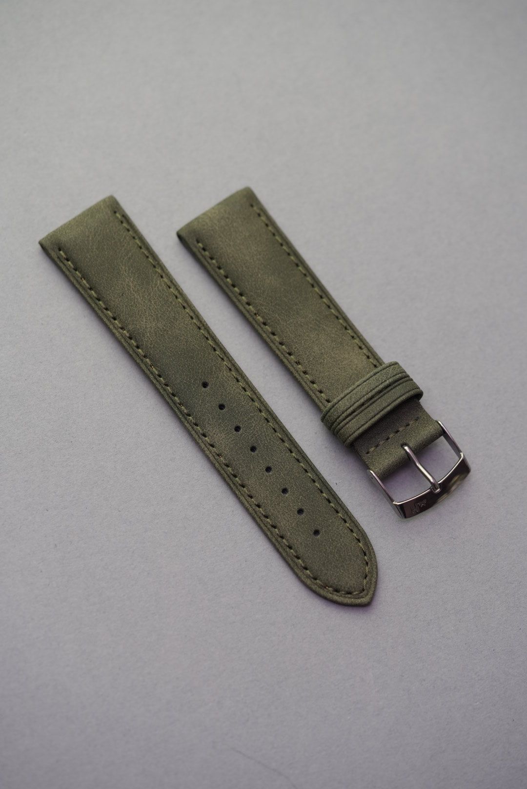 Olive green suede watch strap laid flat, showing full buckle and holes.