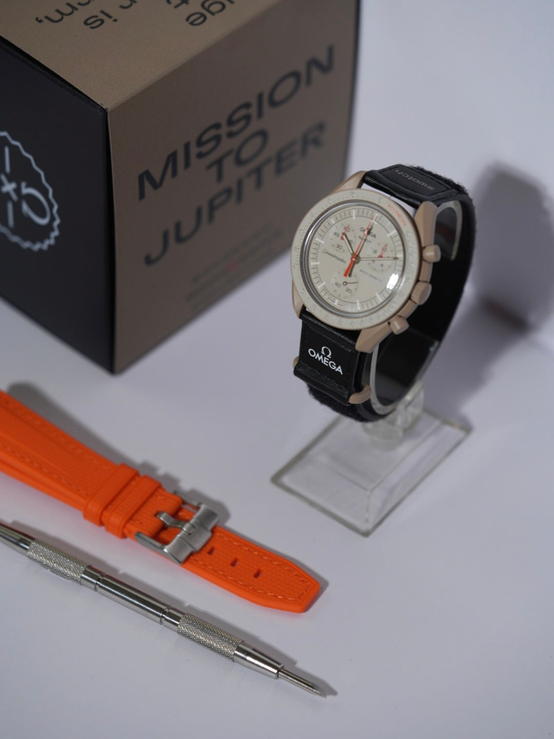 Swatch x Omega MoonSwatch Mission to Jupiter bundle featuring the Jupiter watch, an orange rubber strap, and a spring bar tool, displayed with its packaging.