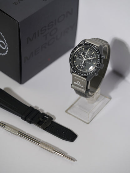 Swatch x Omega MoonSwatch Mission to Mercury bundle featuring the Mercury watch, a black rubber strap, and a spring bar tool, displayed with its packaging.