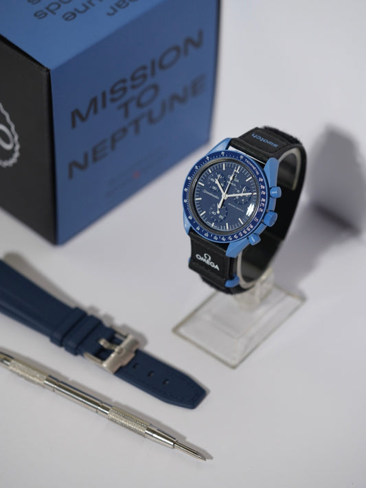 Swatch x Omega MoonSwatch Mission to Neptune bundle featuring the Neptune watch, a navy blue rubber strap, and a spring bar tool, displayed with its packaging.