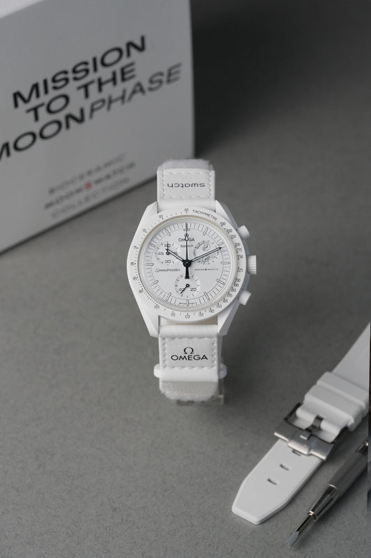 Omega MoonSwatch with white strap on a gray surface, branded packaging in the background.