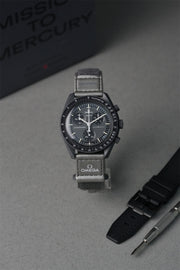 Swatch x Omega Mercury MoonSwatch with grey strap on a grey surface, with 'Mission to Mercury' text in the background.