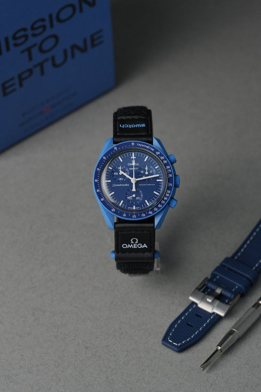 Blue Omega watch with black strap on a gray surface, with 'Mission to Neptune' text in the background.