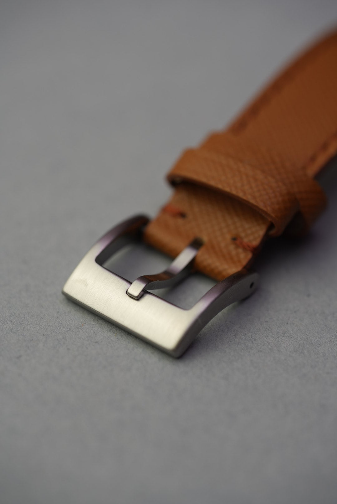 Macro shot of the brushed stainless steel buckle on the tan Saffiano leather strap.