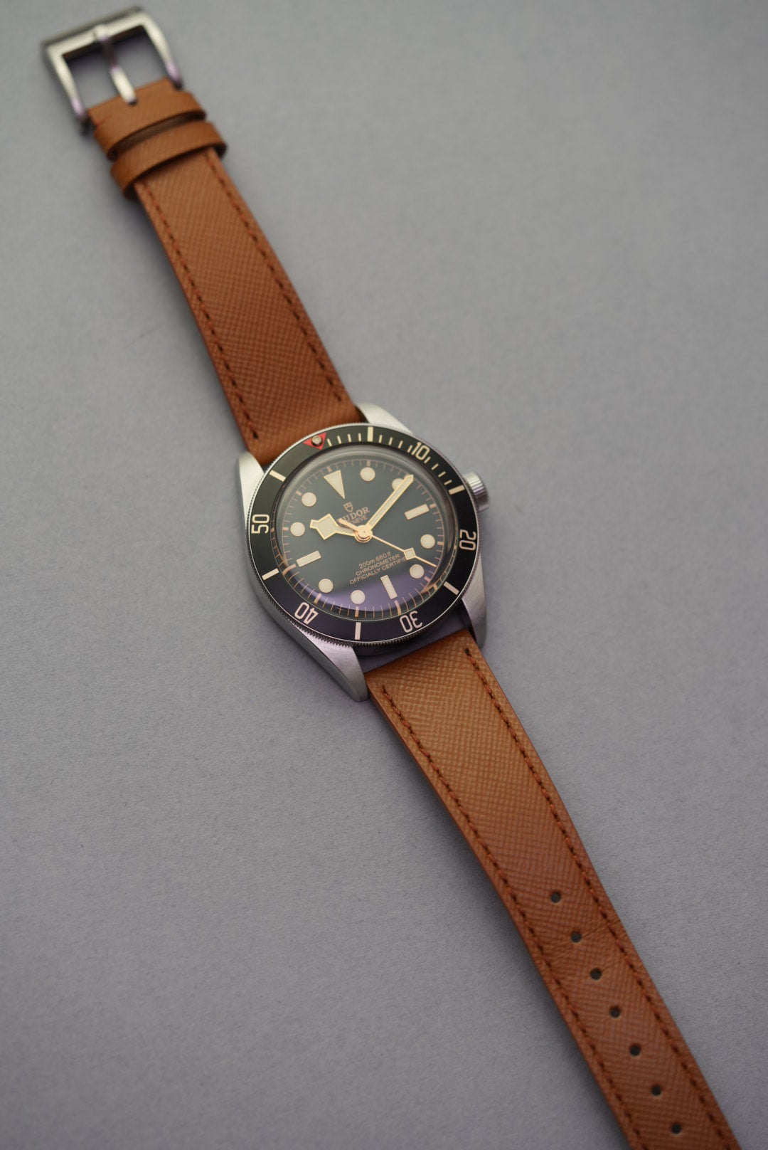 Angled top-down view of a Tudor watch with tan Saffiano strap, highlighting stitching and dial detail
