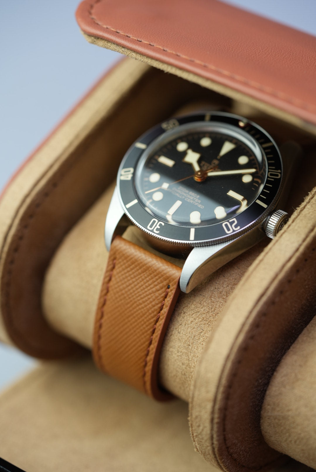 Detailed view of Tudor Black Bay on tan leather strap placed in one slot of the open watch roll.