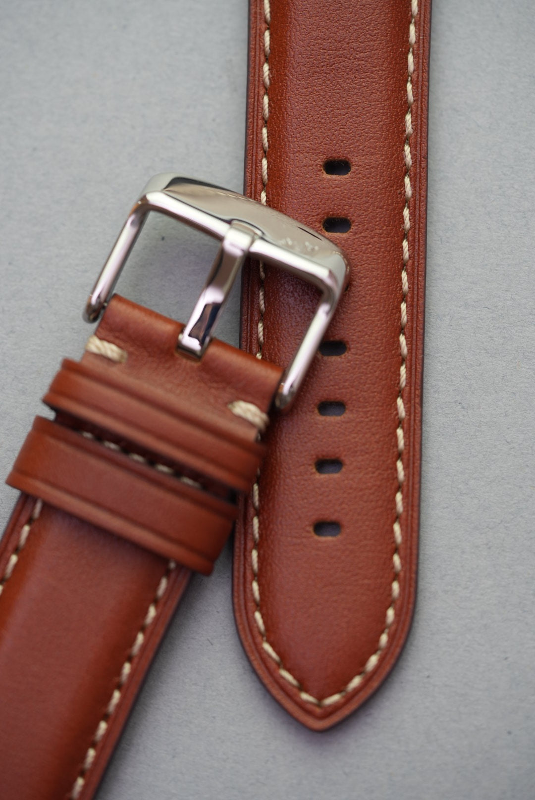 Close-up of tan leather strap with polished buckle and cream stitching