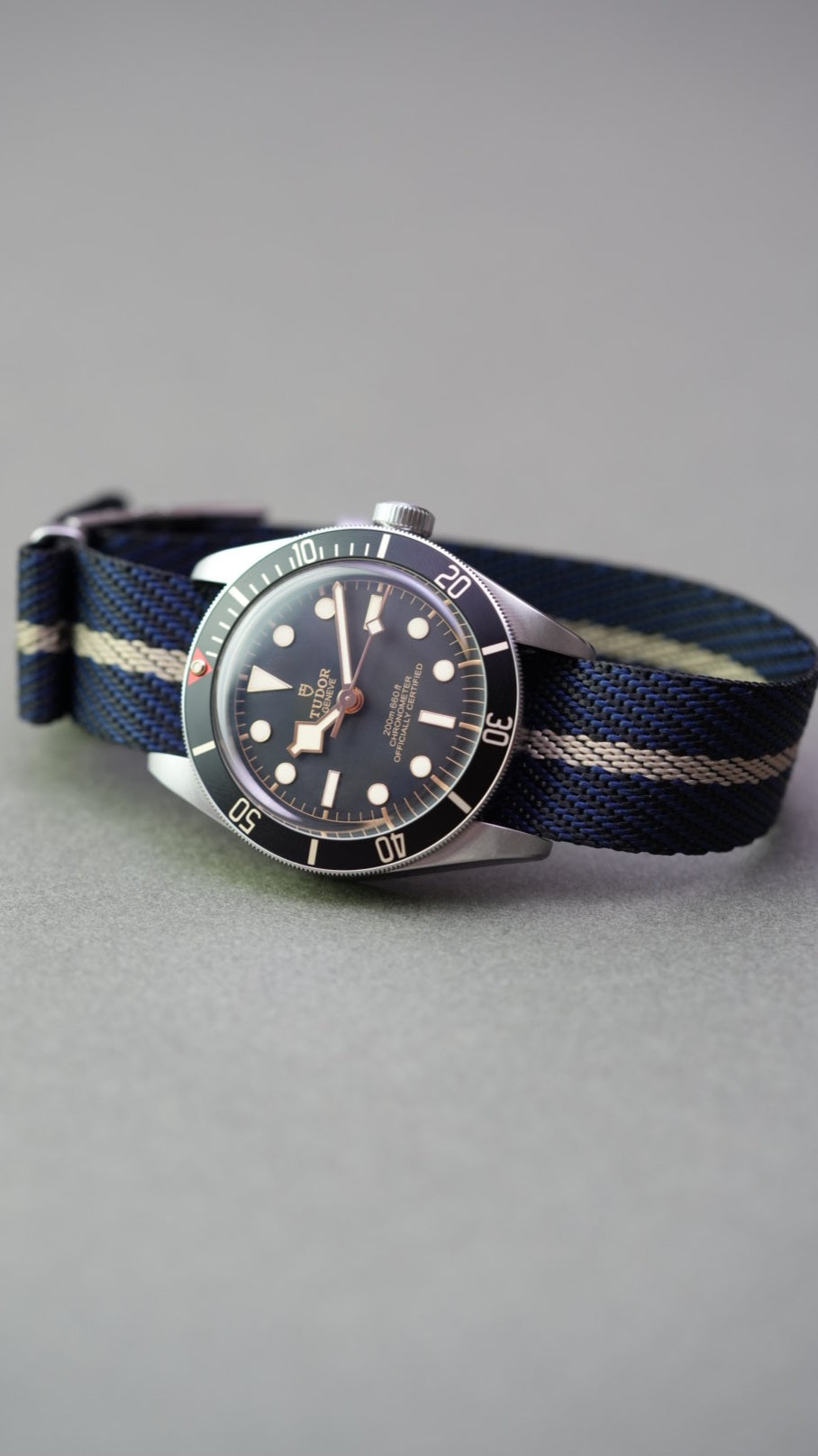 Close-up of brushed steel buckle and punch holes on black, blue, and cream single-pass woven nylon strap.