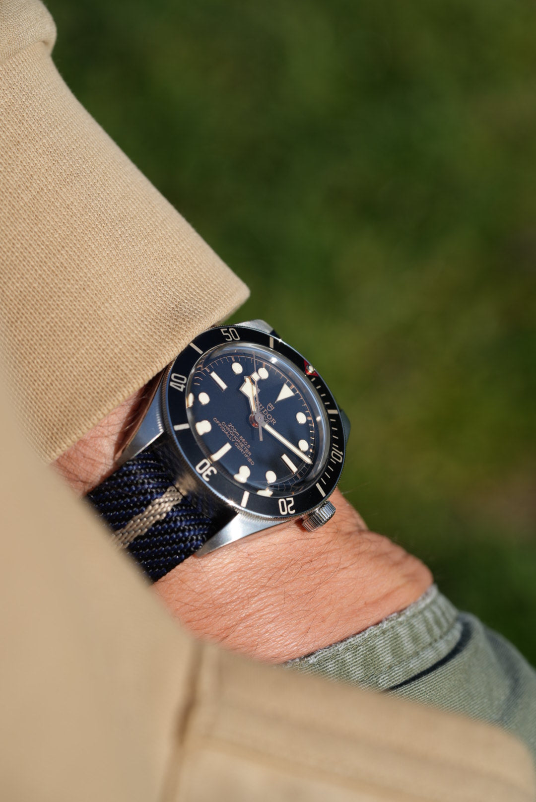 Side angle of Tudor Black Bay worn with black, blue, and cream nylon strap, sleeve and background in focus.