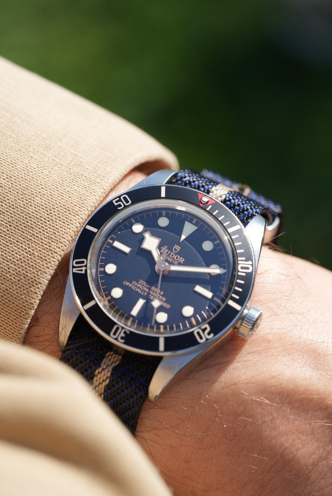 Tudor Black Bay watch worn on wrist in sunlight, fitted with a black, blue, and cream woven nylon strap.
