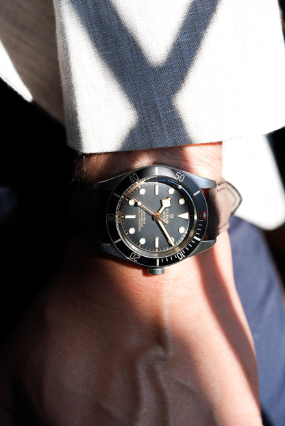 Tudor Black Bay watch with dark brown suede strap in natural lighting, styled with a light linen shirt