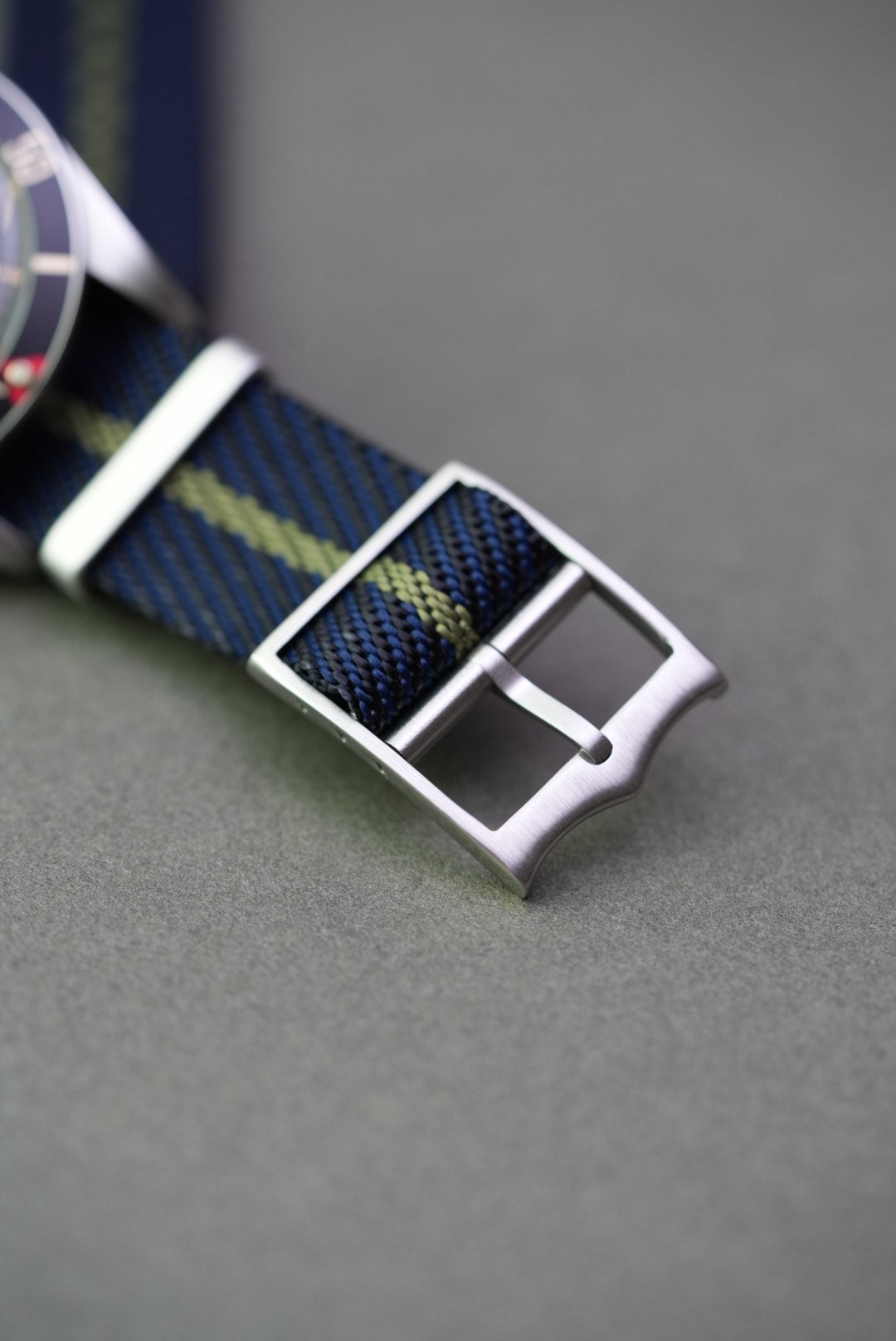 Close-up of brushed buckle and punched holes on green nylon strap with yellow stripe.