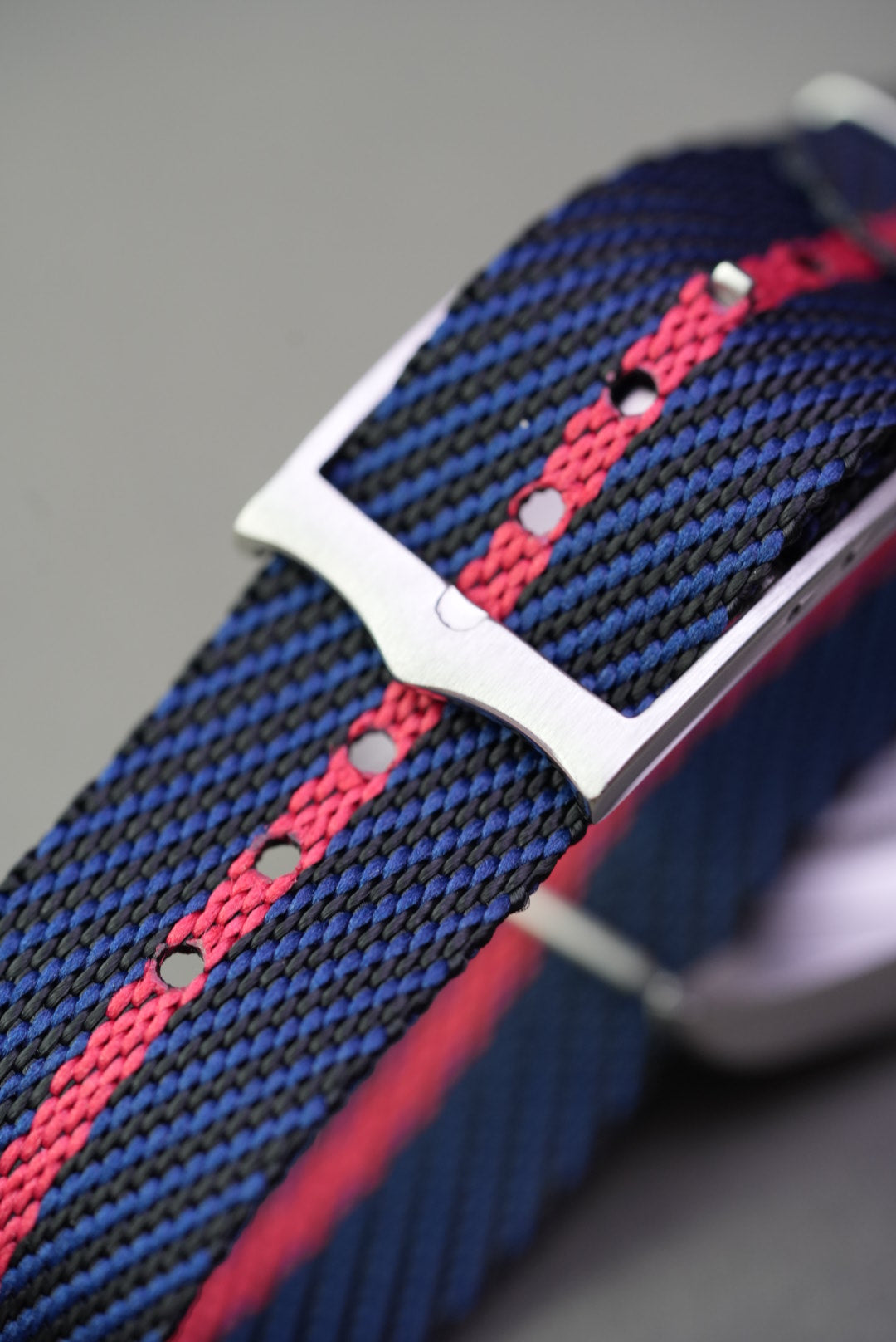 Macro view of brushed steel buckle and punch holes on navy and red woven nylon strap fitted to a Tudor Black Bay