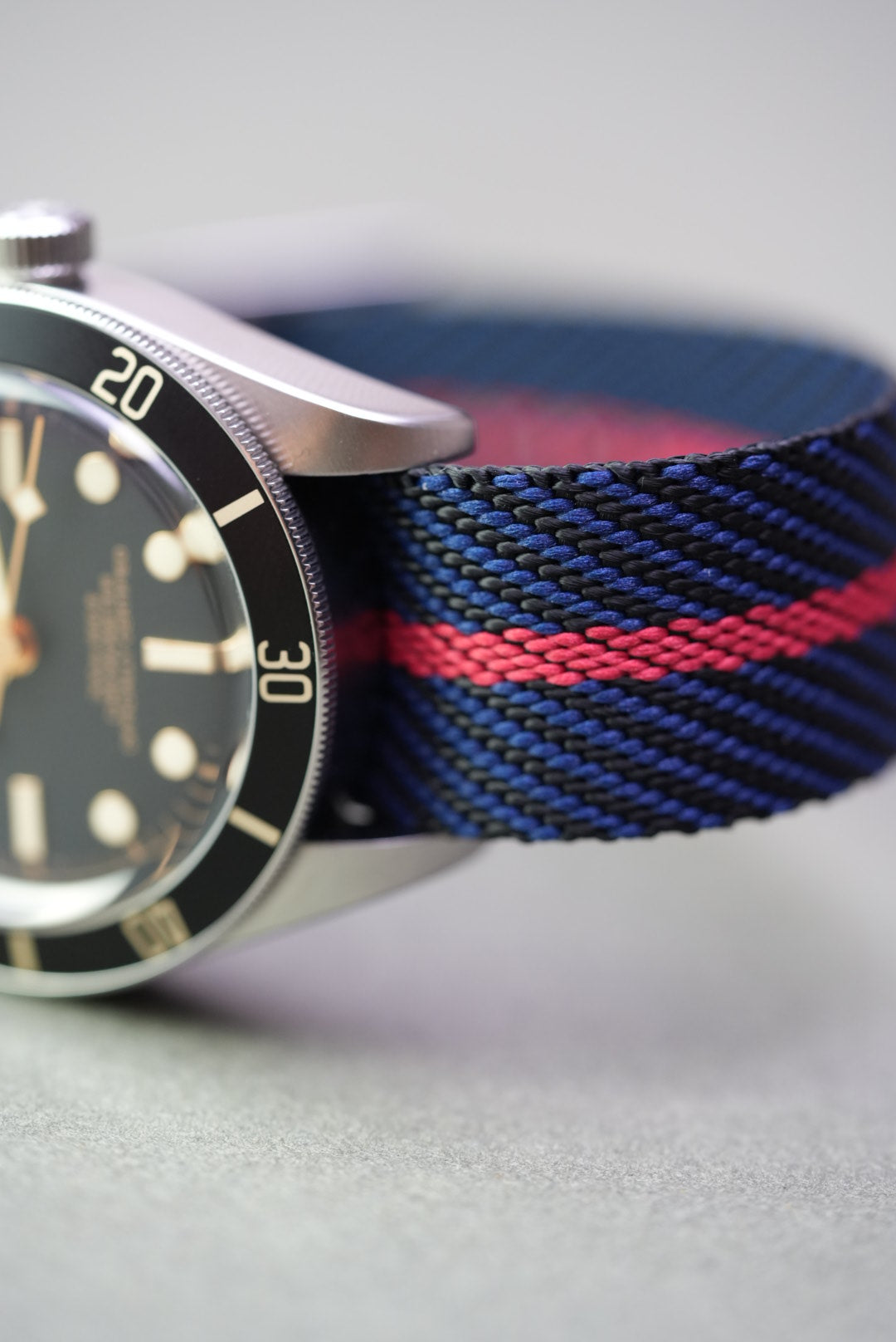 Close-up of navy woven nylon watch strap with red centre stripe on a Tudor Black Bay watch.