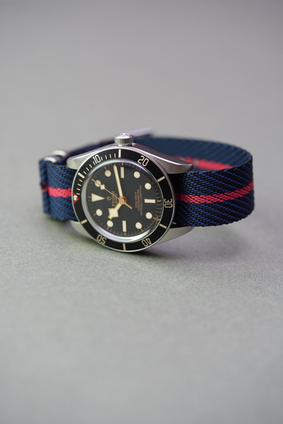 Tudor Black Bay watch on a navy woven nylon strap with a red centre stripe, shown from front angle.