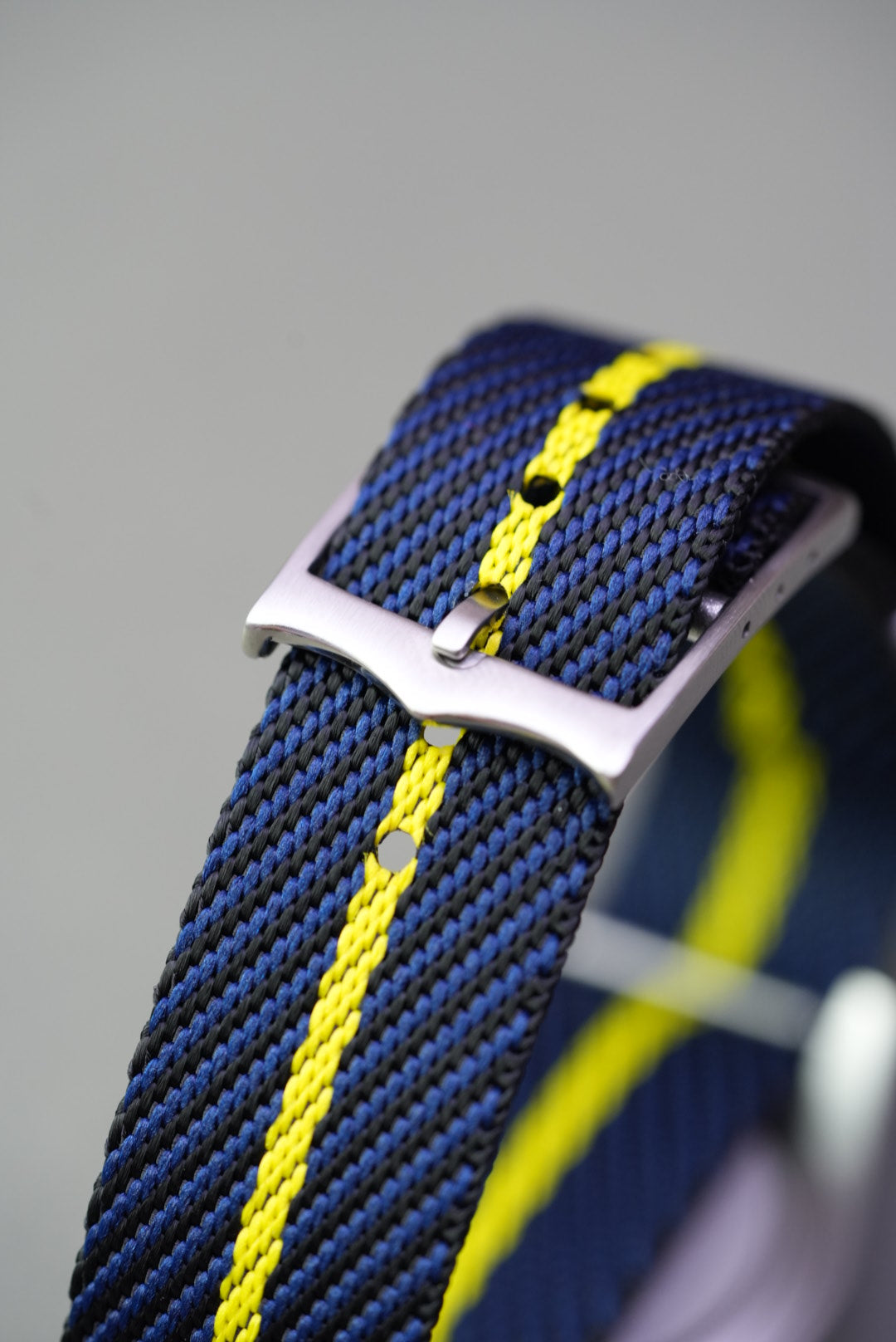 Close-up of brushed buckle and punched holes on navy nylon strap with yellow stripe.