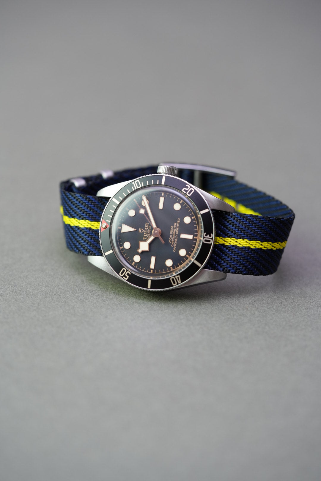 Tudor Black Bay on a navy woven nylon strap with a bold yellow centre stripe, shown from front angle.