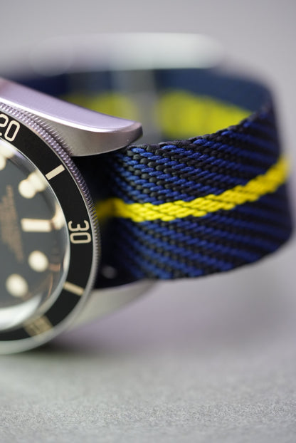 Macro detail of the yellow stripe and woven texture on navy nylon strap attached to a Tudor Black Bay.