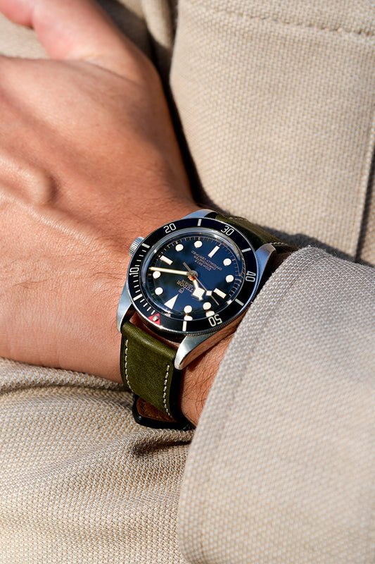Close-up of a wrist wearing a watch with a dark blue face and green leather strap.