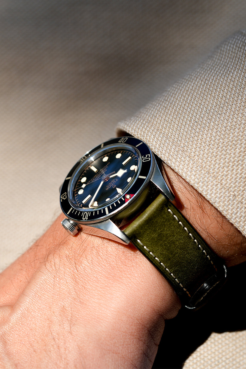 Wrist wearing a watch with a green strap on a neutral background