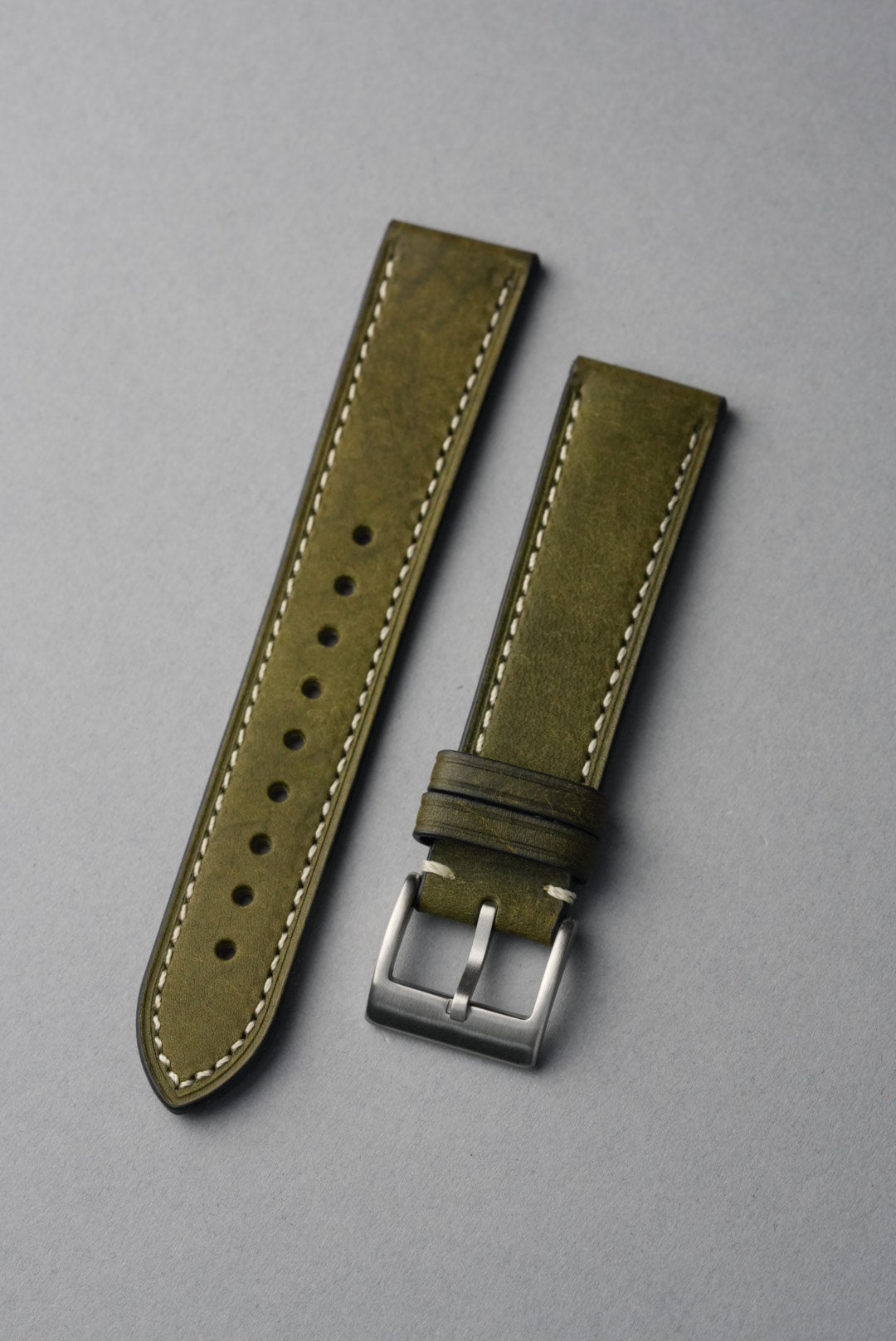 Green leather watch strap with silver buckle on a gray background