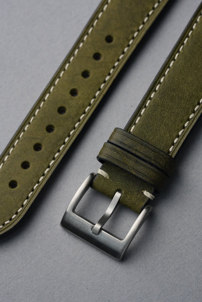 Green leather watch strap with silver buckle on a gray background