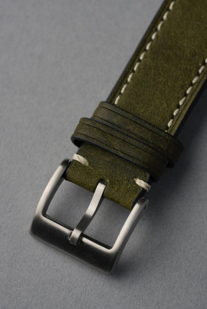 Green leather watch strap with silver buckle on a gray background