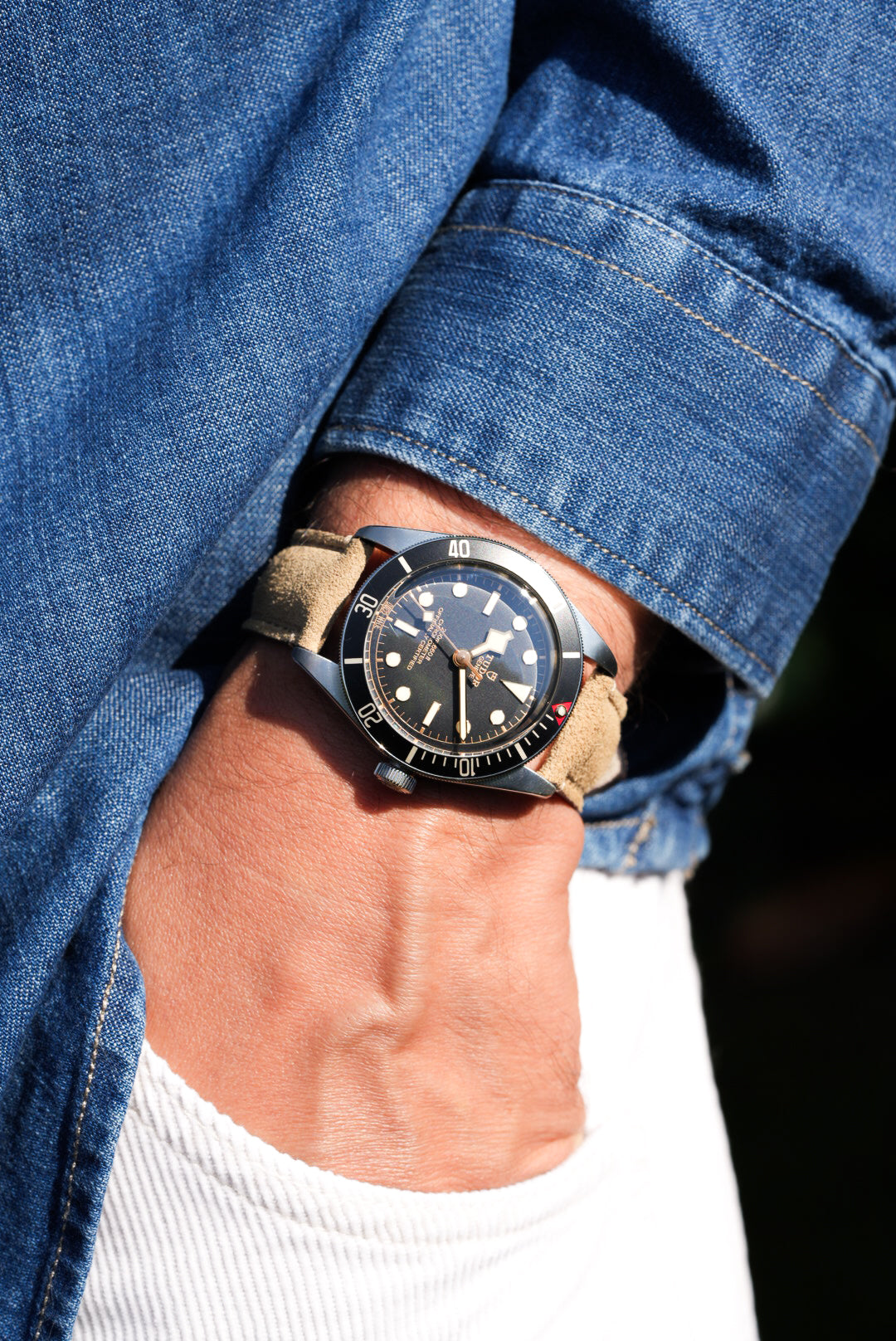 Tudor Black Bay watch with beige suede leather strap, worn on wrist with denim shirt and white jeans