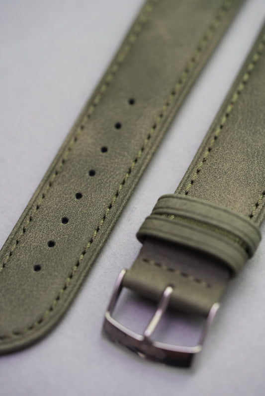 Olive green suede watch strap with polished buckle, viewed from an angle.