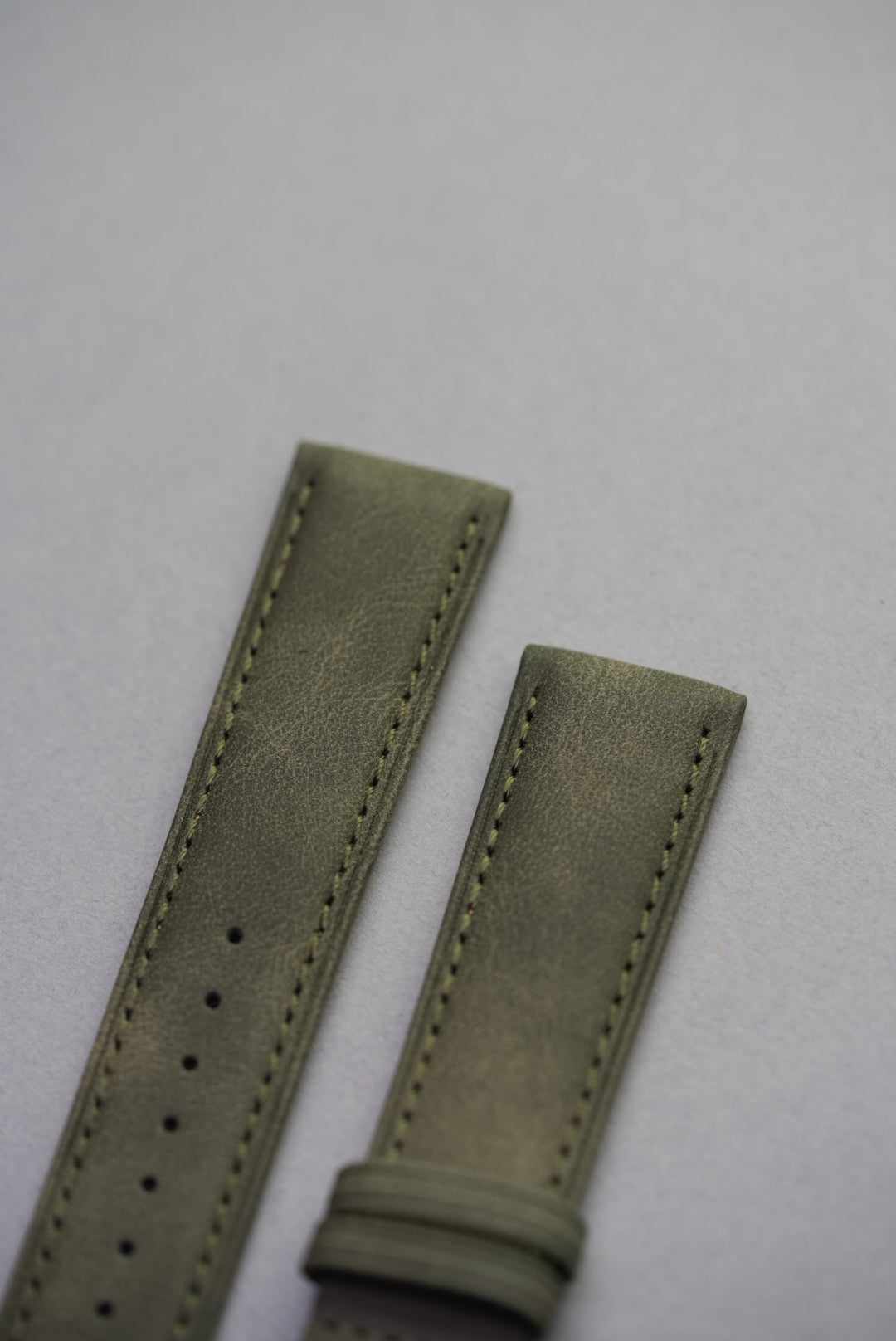  Detailed top-end view of olive green suede strap showing texture and stitching.